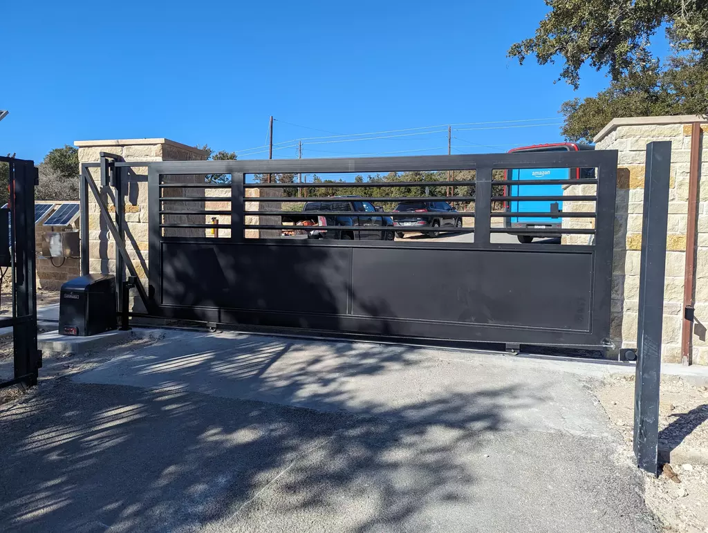 Modern metal dark gray gate that slides on a track to open. Solid bottom half with bars on top half with a flat top