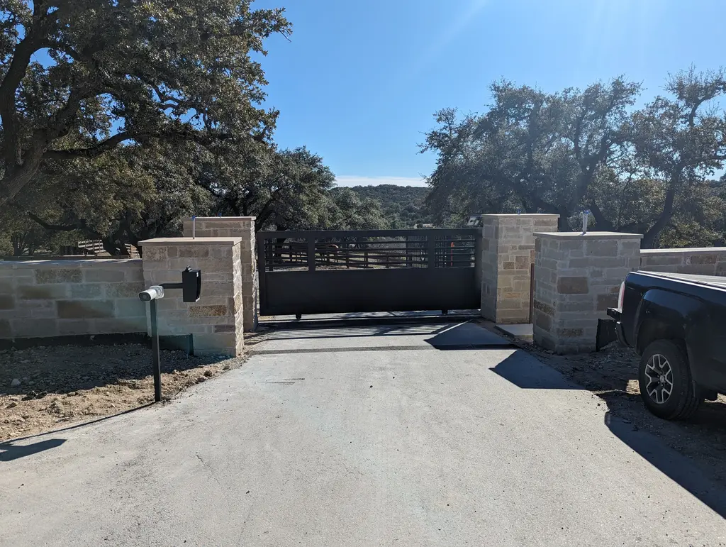 closed black automatic gate with stone facade posts. camera and electronic keypad on black steel post in foreground