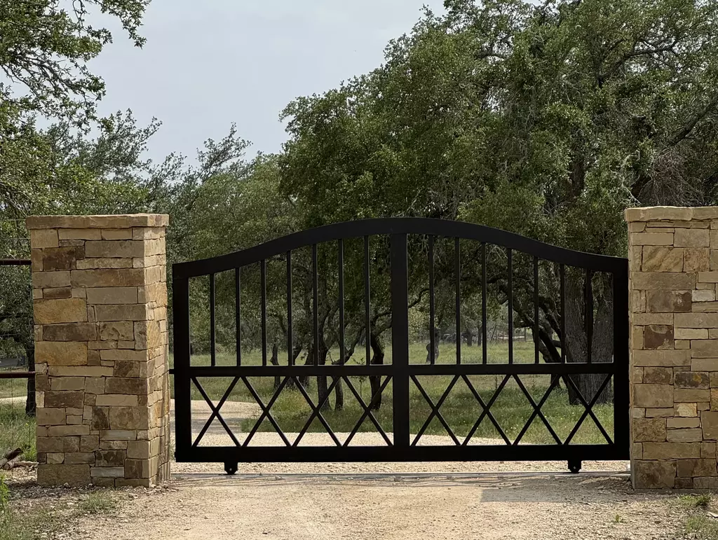 Black metal bell arched swing gate with two stone pillars in brown stone 