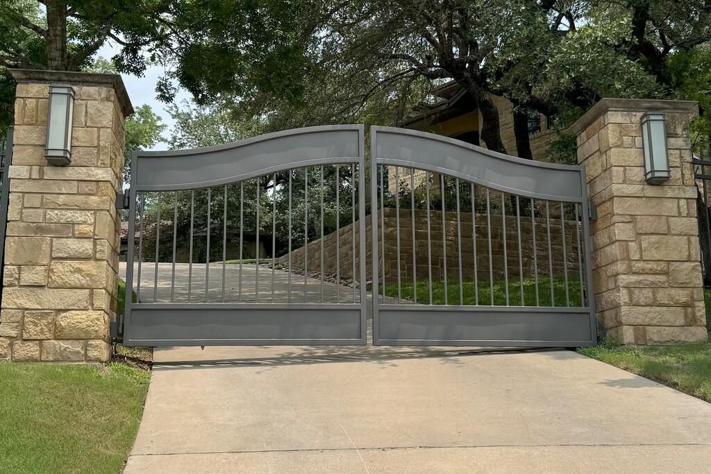 Gray Metal bell arched swing gate with beige stone pillars on either side